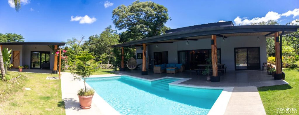 View of main house of equestrian estate listed by Discover Real Estate across pool with view of one casita bedroom