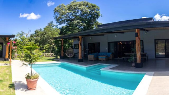 View of main house of equestrian estate listed by Discover Real Estate across pool with view of one casita bedroom