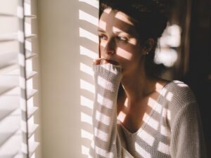 When T4 Isn’t Enough T3 Deficiency & Thyroid Disease Part 1: Image of a meloncholy woman in a sweater looking out of the window.